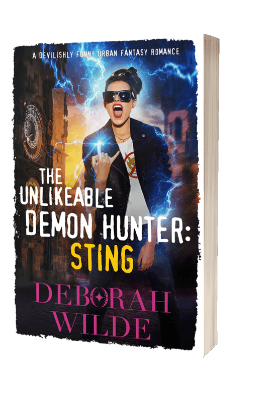 Paperback cover for "The Unlikeable Demon Hunter:Sting", by Deborah Wilde. A brunette in sunglasses, wearing a "no demons" t-shirt flashes devil horns with her hand as lightning sparks around her.