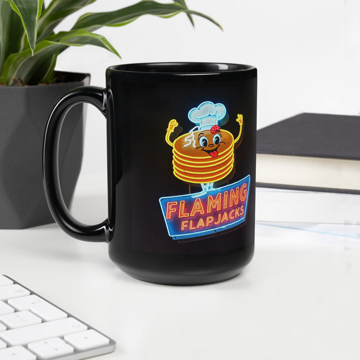 Black ceramic mug with neon sign of "Flaming Flapjacks" logo. A smailing cartoon stack of pancakes with a chef hat and arms.