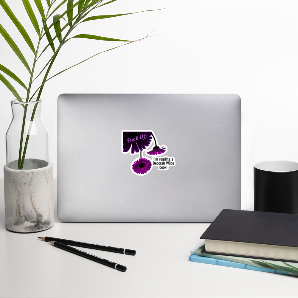 A laptop computer has a kiss cut sticker with purple daisies and the text "Fuck off. I'm reading a Deborah Wilde book!