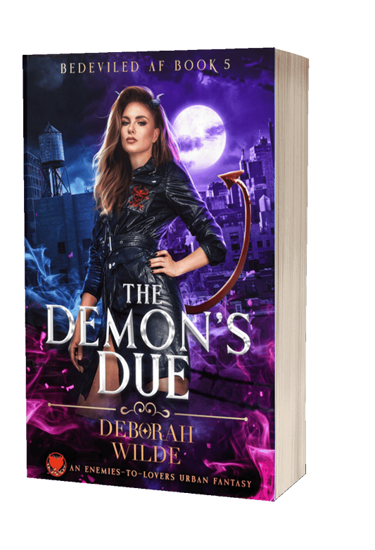Paperback cover of "The Demon's Due" featuring a woman in a black leather trench coat with horns and a tail standing in front of a city at night.